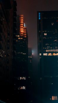 Discover a moody urban night scene featuring illuminated skyscrapers and a misty atmosphere.