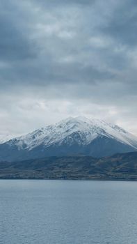 Snowcapped mountain under cloudy winter sky in Van, Turkey, overlooking a tranquil lake.