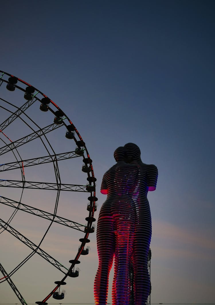 Ali And Nino Sculpture And A Ferris Wheel In The Background At Sunset 