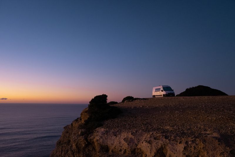 A tranquil van parked on a cliff overlooking the ocean at sunset