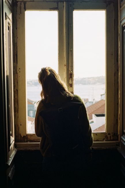 Silhouette of a woman standing by a window in Lisbon, overlooking the cityscape.