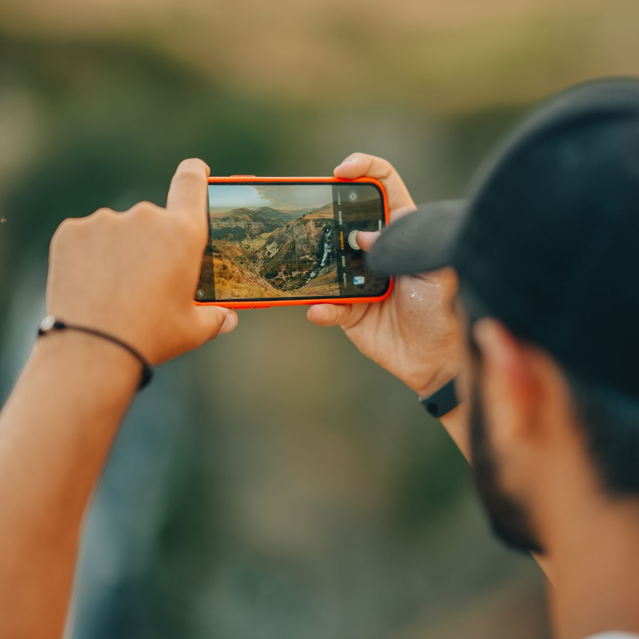A man using a smartphone to photograph a scenic mountain view