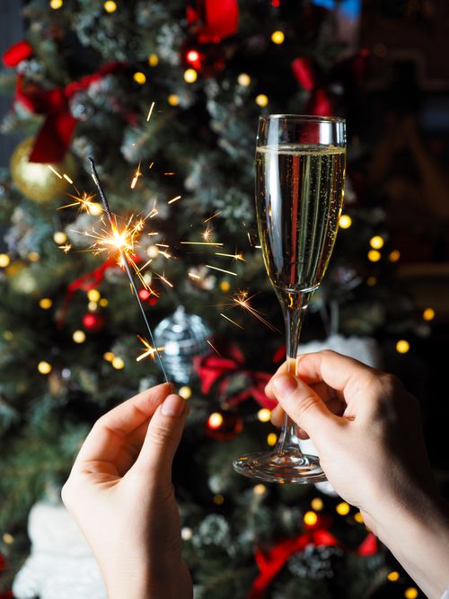 Free Celebrate with champagne and sparkler in front of a decorated Christmas tree. Perfect holiday vibe. Stock Photo