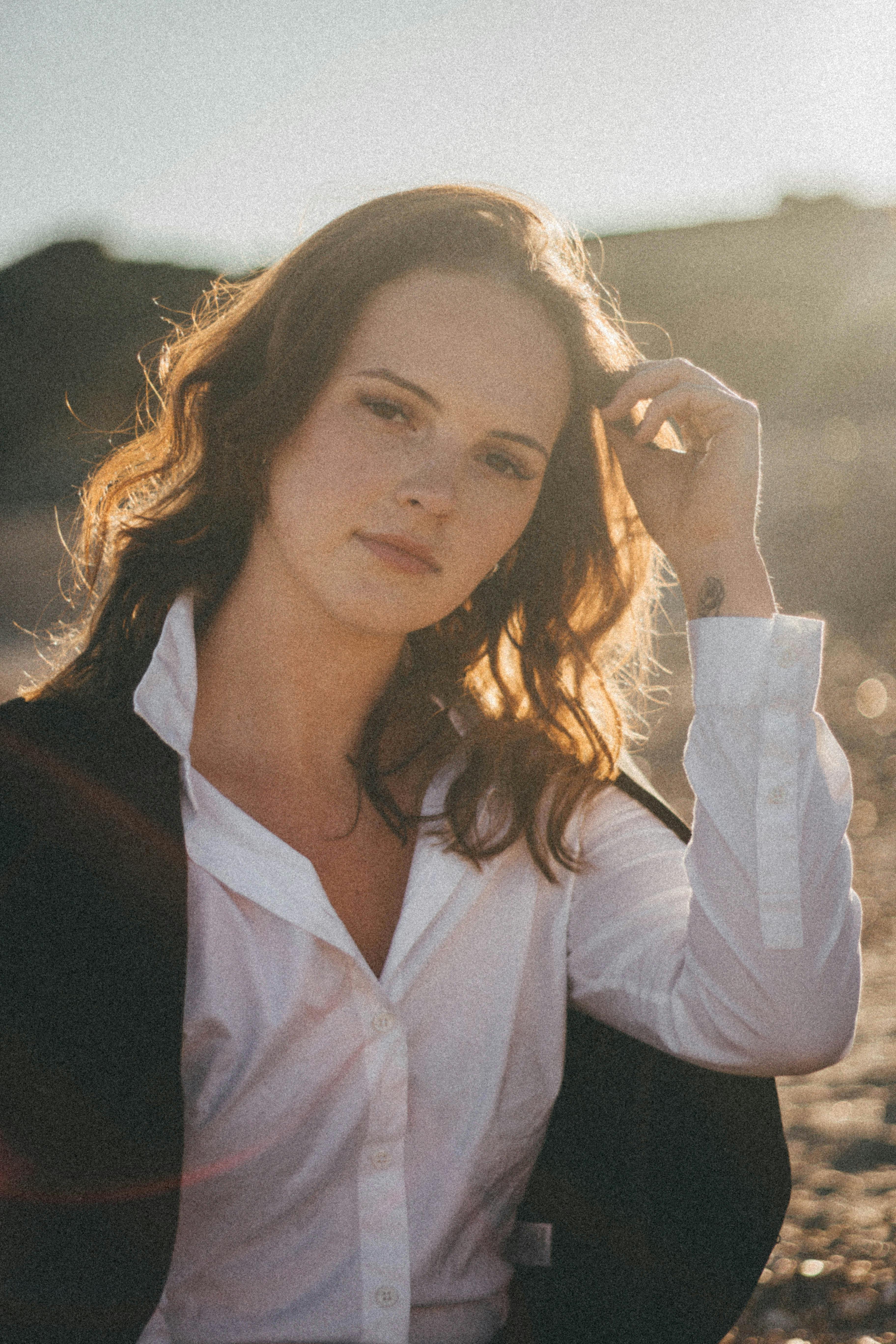 A beautiful woman poses outdoors with sunlight highlighting her features, conveying elegance and confidence.