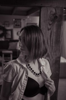 A black and white portrait of a woman in an open shirt and necklace indoors, exuding elegance.