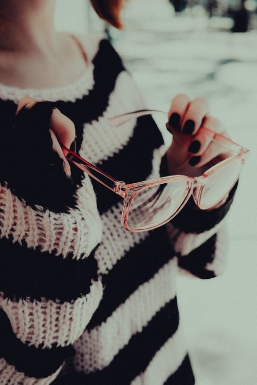 Free Close-up of a woman holding eyeglasses, wearing a stylish black and white striped sweater. Stock Photo