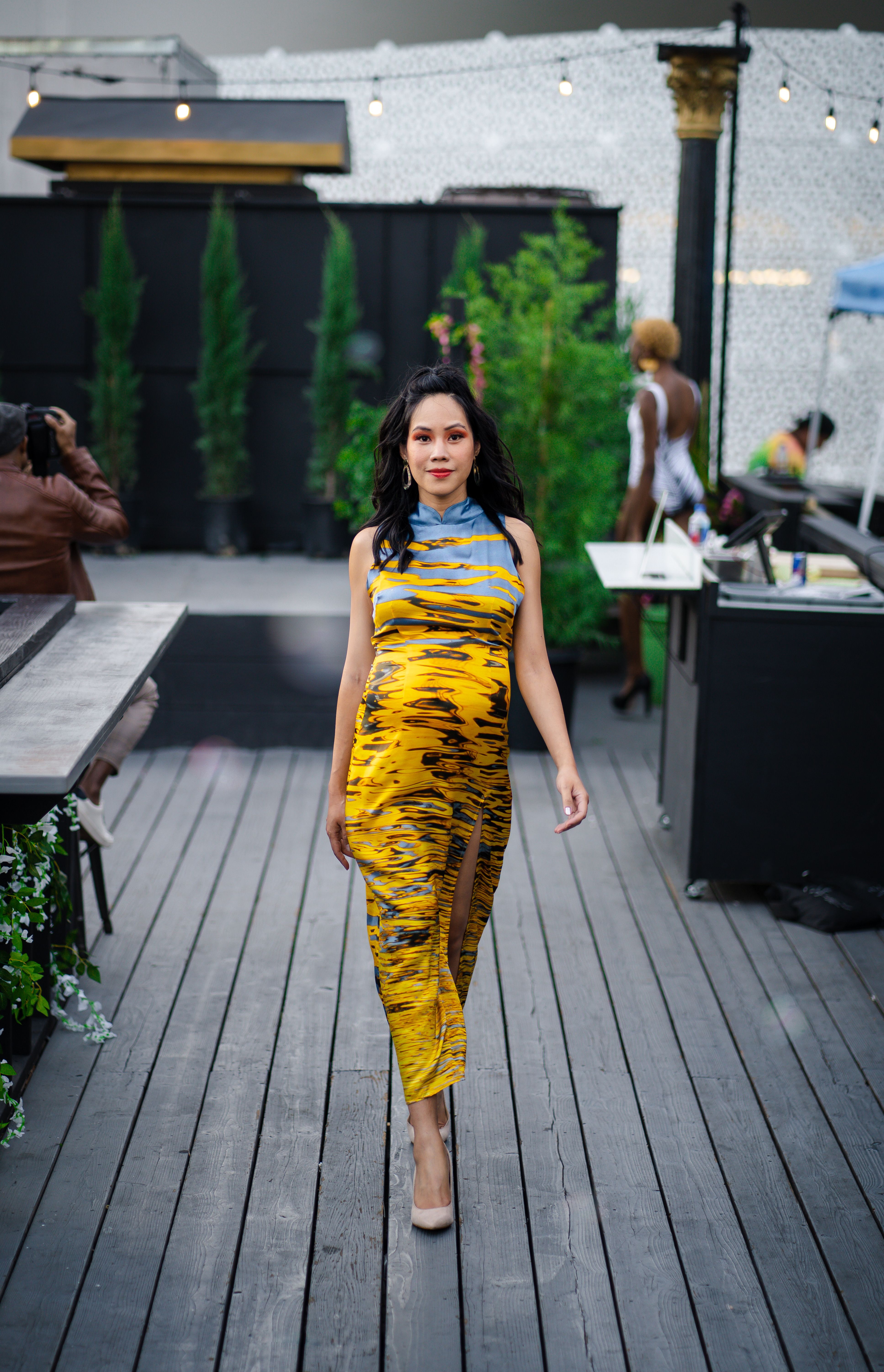 Stylish woman in a yellow dress walking on a deck, showcasing fashion and elegance.