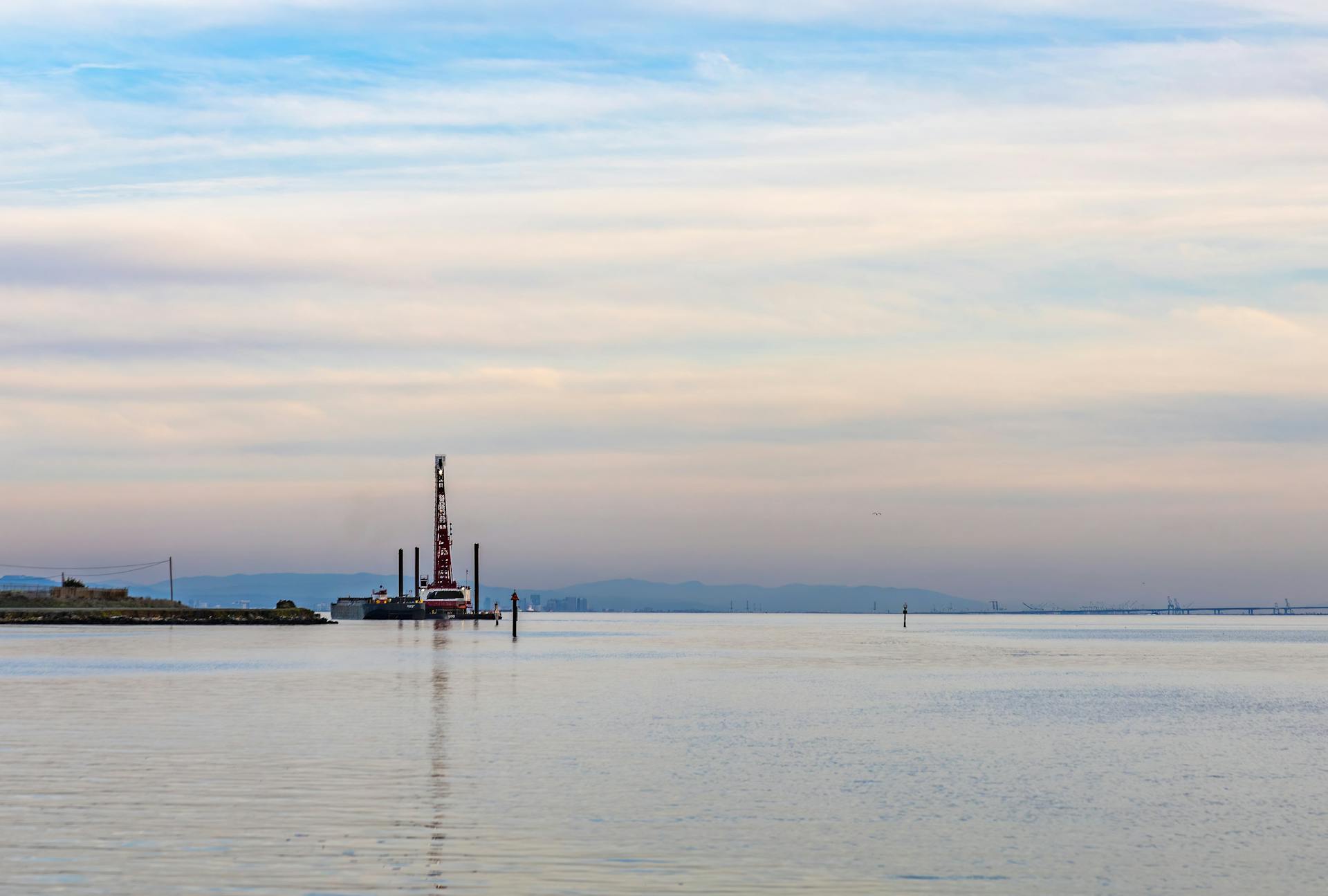 Serene coastal landscape featuring an offshore drilling rig under an expansive sky.