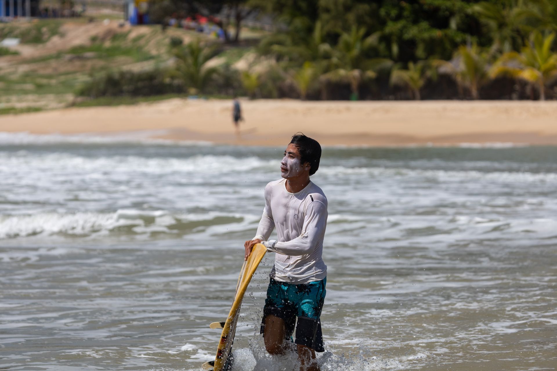 A young surfer with zinc sunscreen runs in the ocean on a sunny beach day.