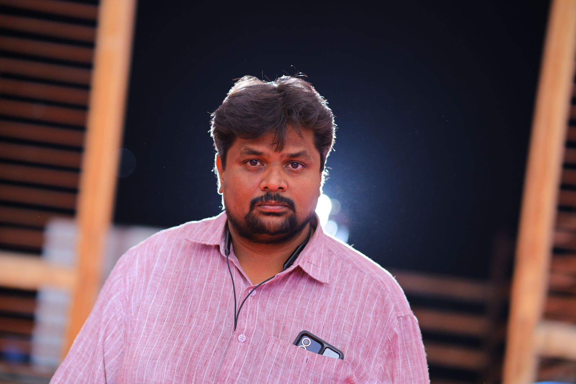 Close-up portrait of an adult man wearing a pink striped shirt, captured outdoors.