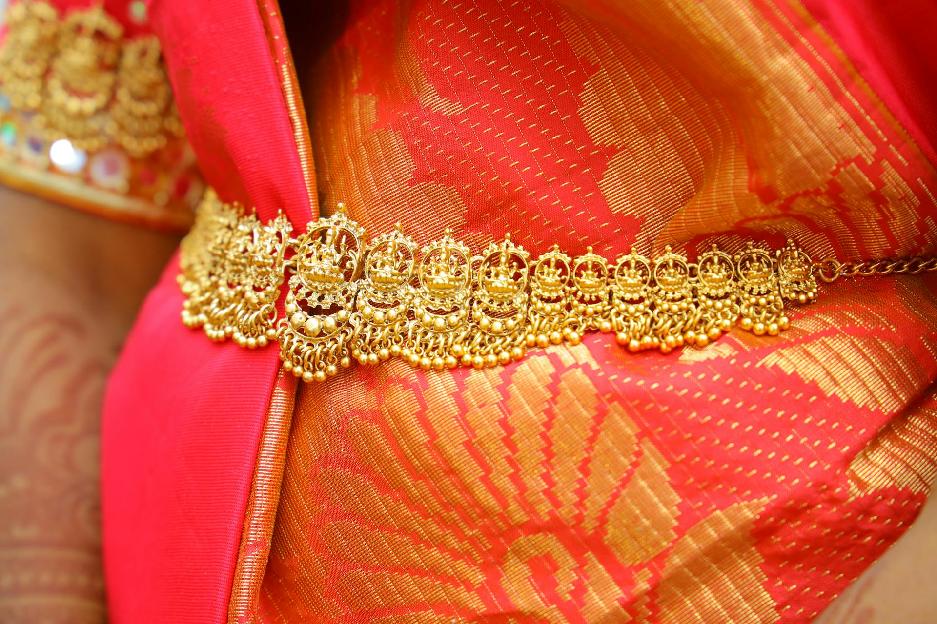 Close-up of an intricate gold waist belt on vibrant traditional sari fabric with rich embroidery.