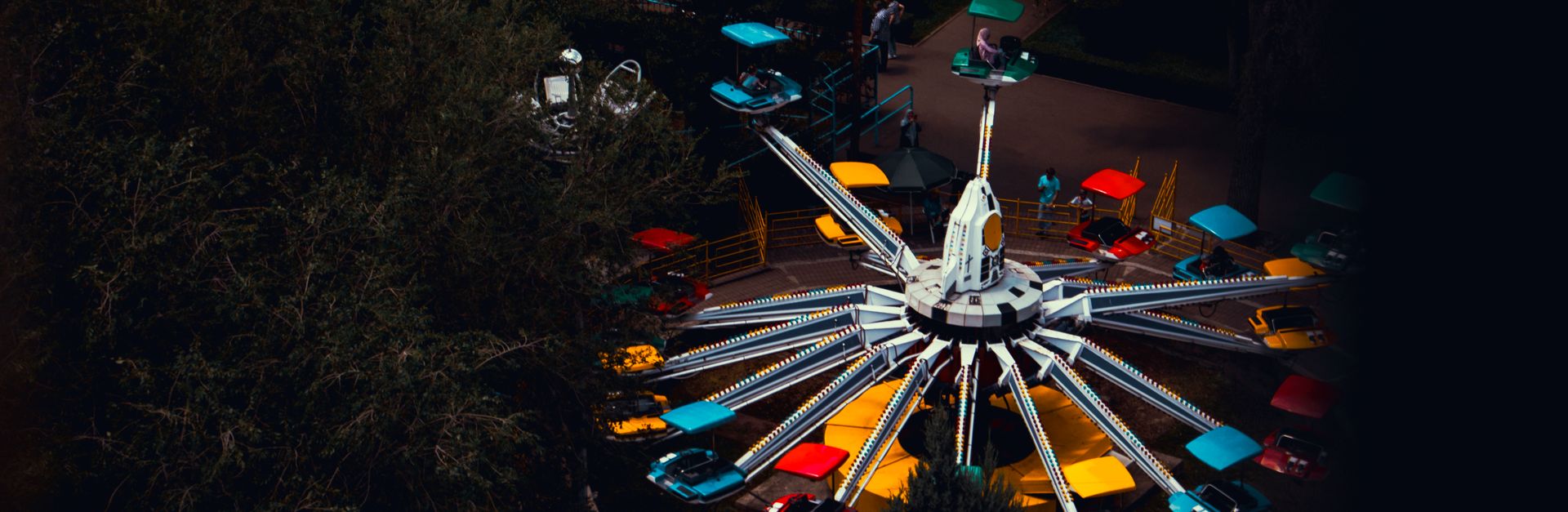 Vibrant amusement park ride captured from above, highlighting bright colors against a dark evening b