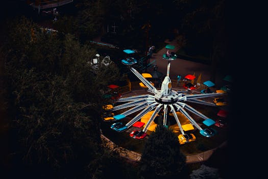 Vibrant amusement park ride captured from above, highlighting bright colors against a dark evening backdrop.