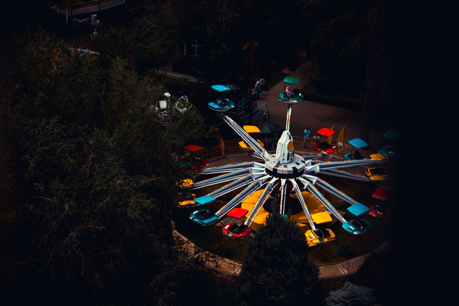 Vibrant amusement park ride captured from above, highlighting bright colors against a dark evening b