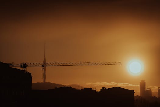 A striking silhouette of a city skyline with a tower crane against a dramatic sunset, perfect for cityscapes.
