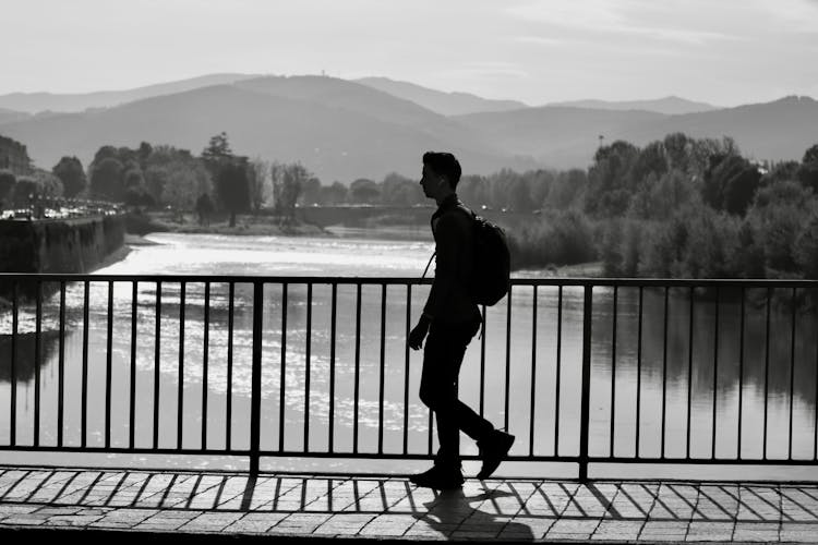 Grayscale Photo Of A Man Walking On The Bridge