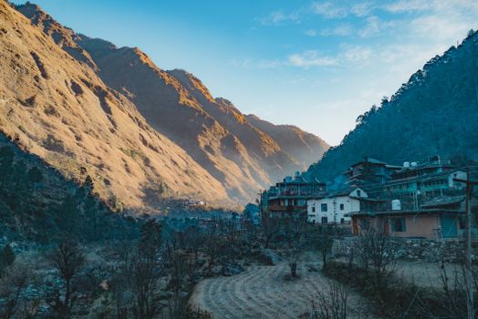 A serene rural village nestled in a sunlit valley surrounded by towering mountains.