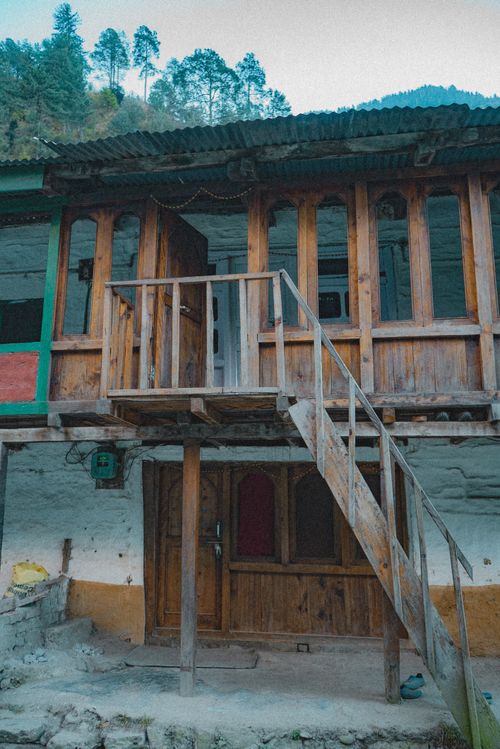 Free An old wooden house with damaged stairs and rustic charm, set against a green forest backdrop. Stock Photo