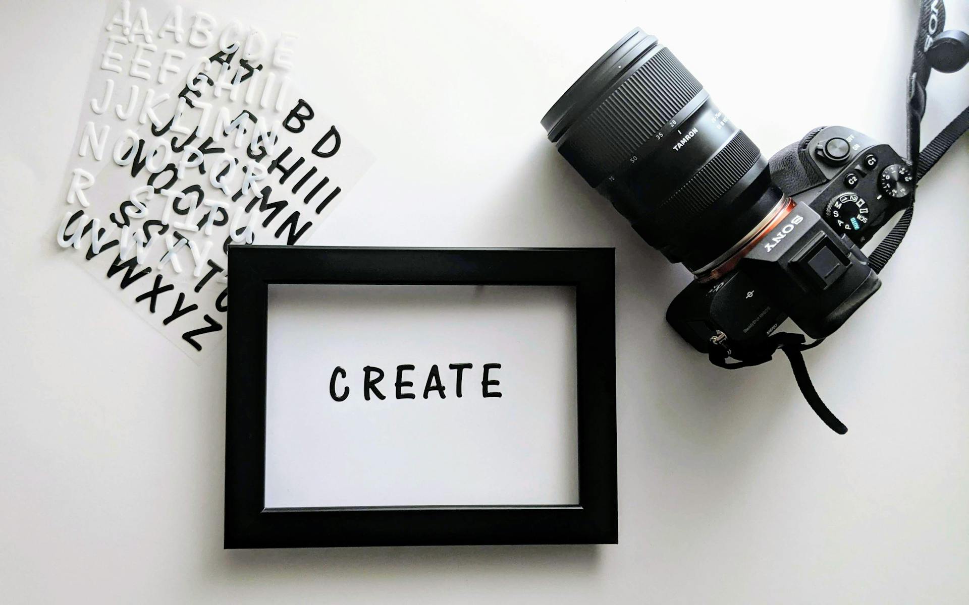 Flat lay image featuring a camera, letter stickers, and a frame with the word 'CREATE' on a white surface.