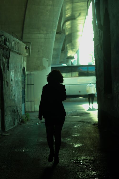 Free Two silhouetted figures walking through a dimly lit urban corridor under an archway. Stock Photo