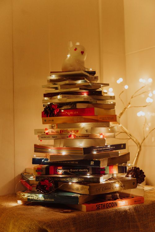 Free A creative Christmas tree made from a stack of books, adorned with string lights and festive decor. Stock Photo