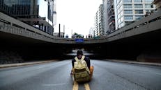 在巴西圣保罗，一名背着背包的男子坐在空荡荡的城市立交桥下的道路上