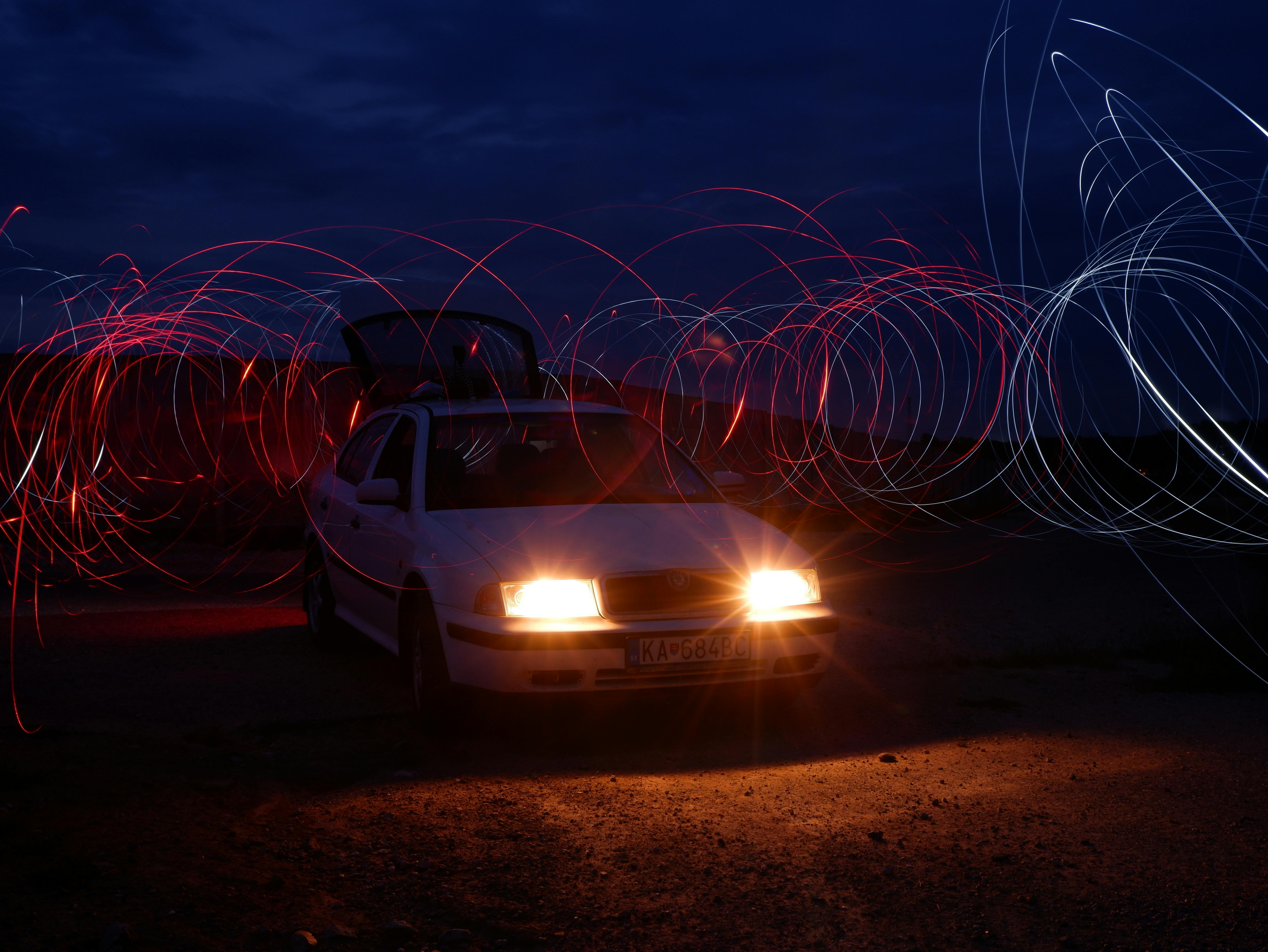 A car parked at night with bright headlights and mesmerizing steel wool light trails.