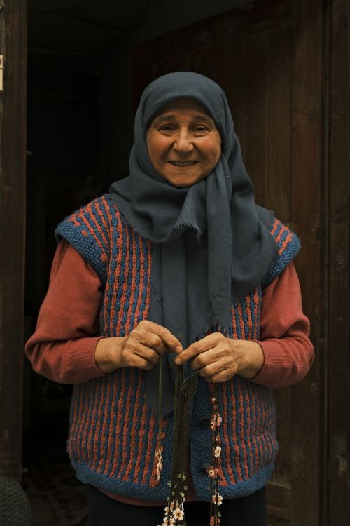 Free Happy senior woman wearing a colorful sweater and headscarf, smiling warmly outdoors. Stock Photo