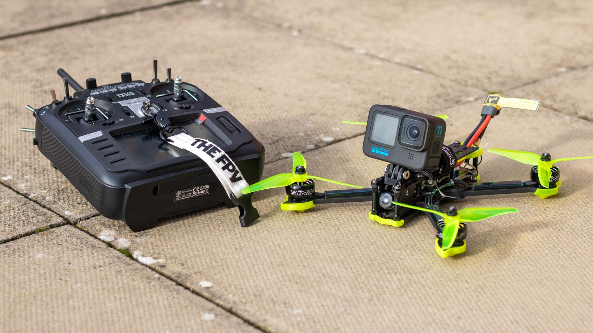 Close-up of FPV drone with action camera and controller on outdoor pavement, ready for flight.