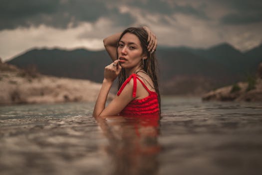 Young woman in red dress posing in a lake with scenic mountain backdrop in Potrerillos, Mendoza.