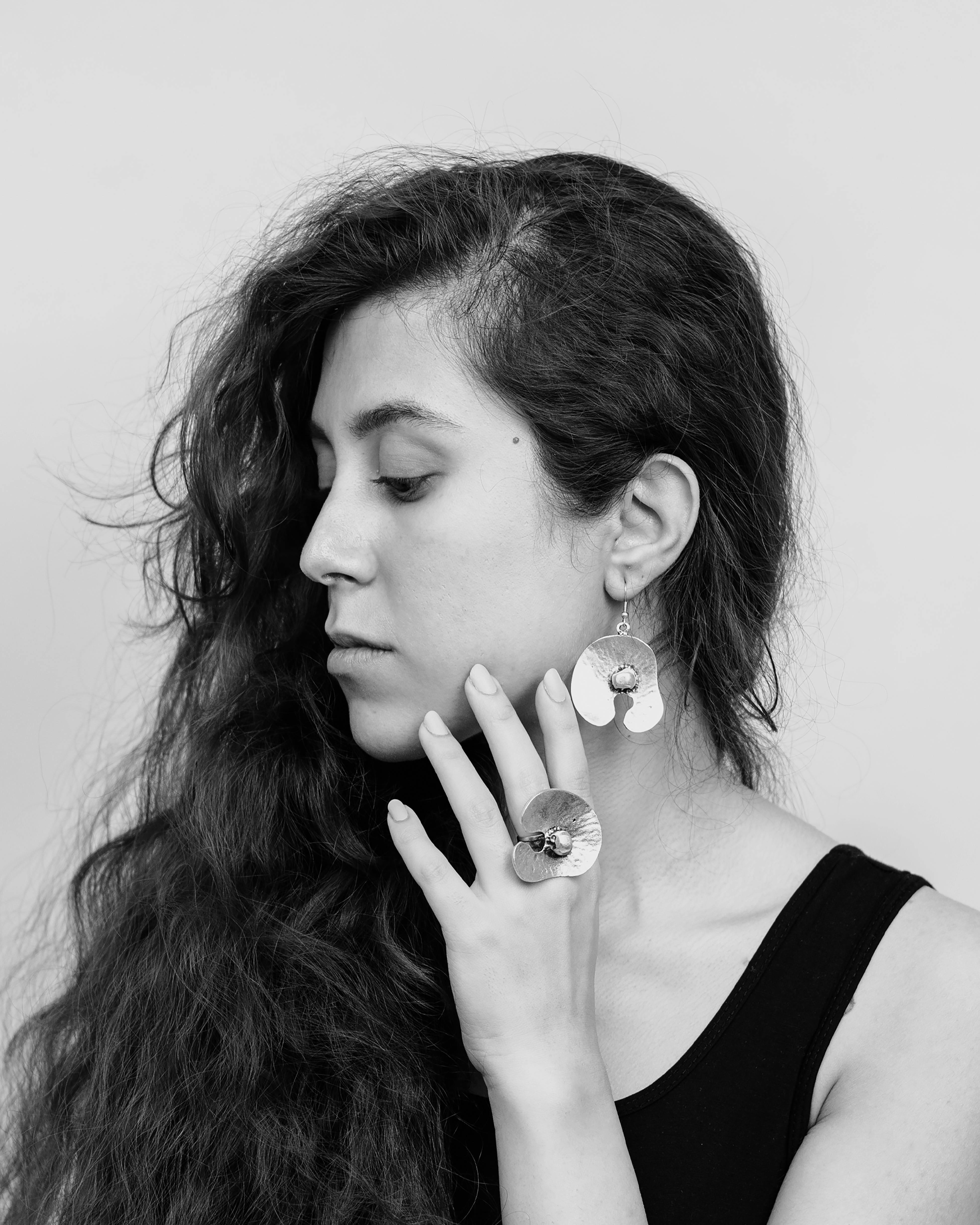 Black and white portrait of a woman wearing bold earrings and rings, gazing sideways.