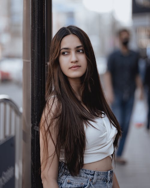 A Long Haired Woman in White Top Leaning on Metal Post