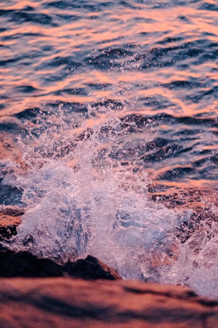 Fotomural Cautivador primer plano de olas rompiendo contra las rocas al atardecer, mostrando la dinámica del agua.