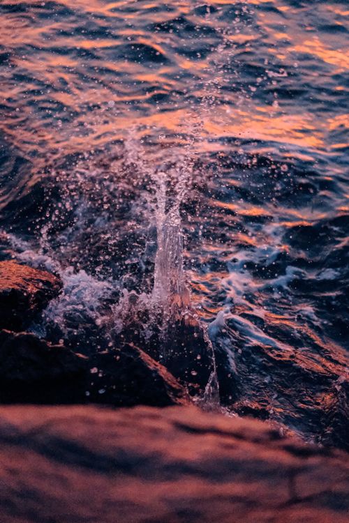 Free Dramatic sunset scene with ocean waves splashing against rocks, capturing nature's beauty. Stock Photo