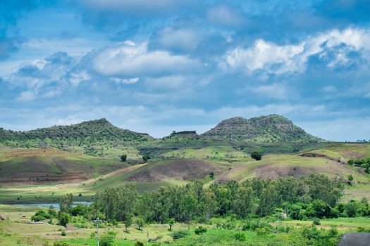 Scenic view of lush green hills and trees beneath a bright blue sky with clouds.