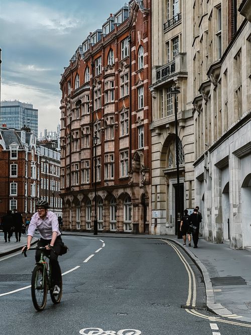 Free A cyclist rides through a historic urban street with striking architecture and city life. Stock Photo