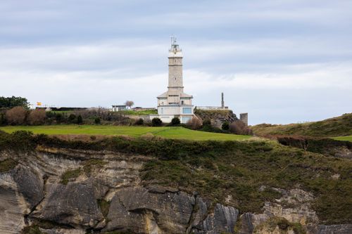 Free Scenic view of a historic lighthouse perched on a rocky coastal cliff under a cloudy sky. Stock Photo