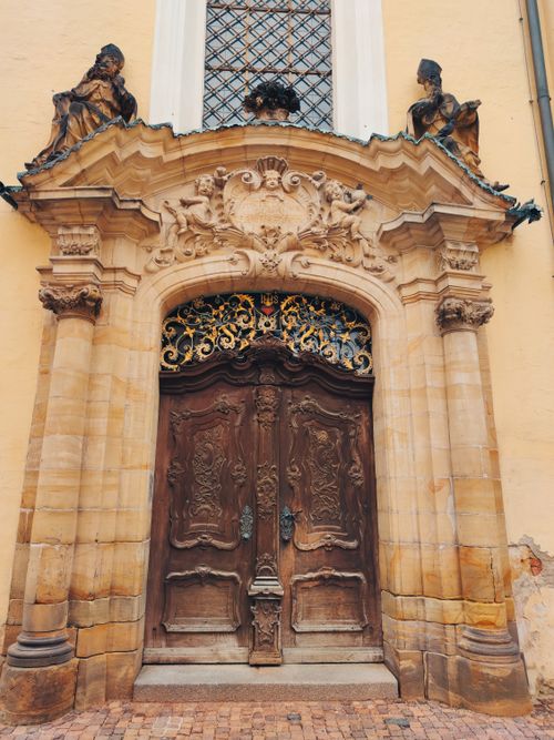 Free Exquisitely carved Baroque palace entrance featuring detailed sculptures and wooden doors. Stock Photo