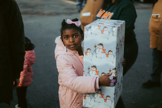 Young girl outdoors holding a large snowman-themed wrapped present during a festive event.