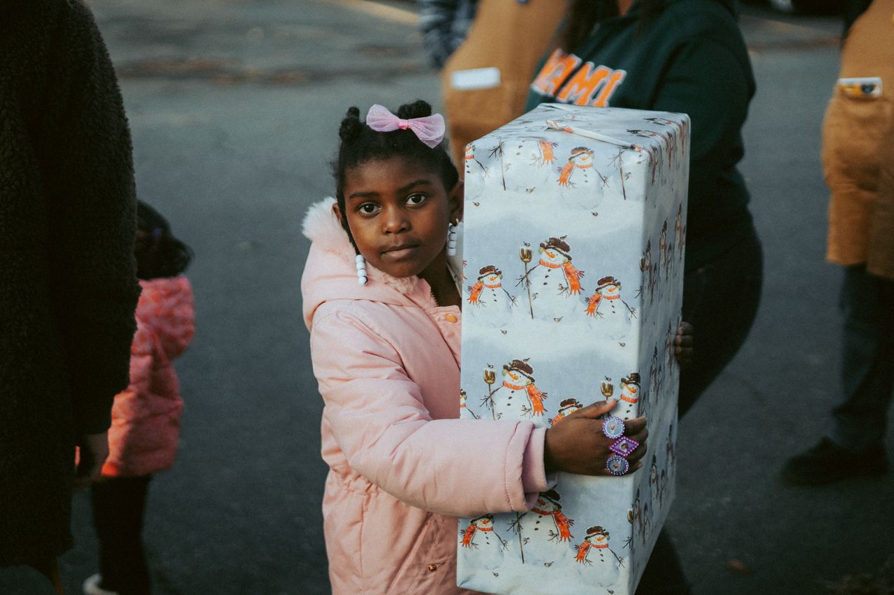 young girl outdoors holding a large snowman themed wrapped present dur