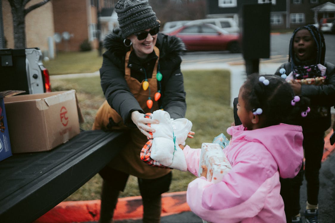 Free Volunteer exchanging holiday gifts with children, spreading festive cheer in a community setting. Stock Photo