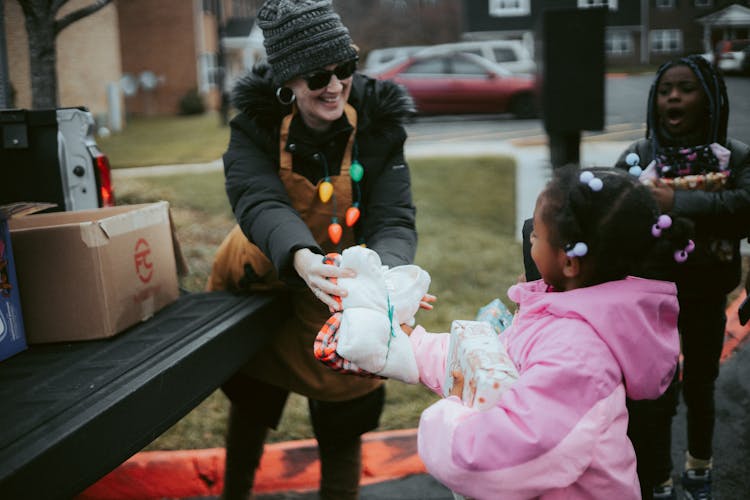 Volunteer In A Christmas Costume Giving A Present To A Little Girl 