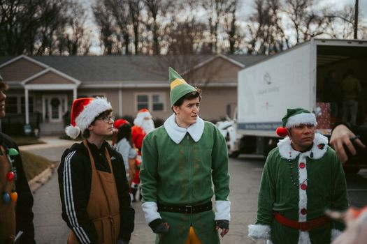 Group of volunteers in elf costumes spreading Christmas cheer by distributing gifts in a neighborhood.