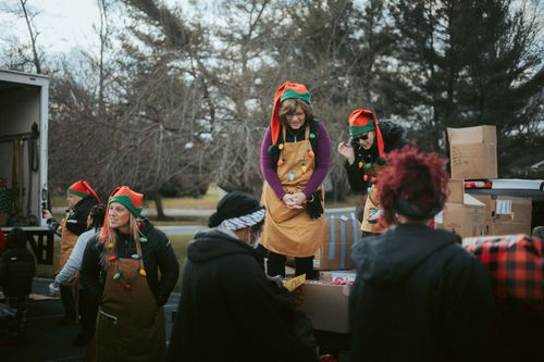 Free Festive volunteers in elf hats distribute gifts from a truck during a community event. Stock Photo