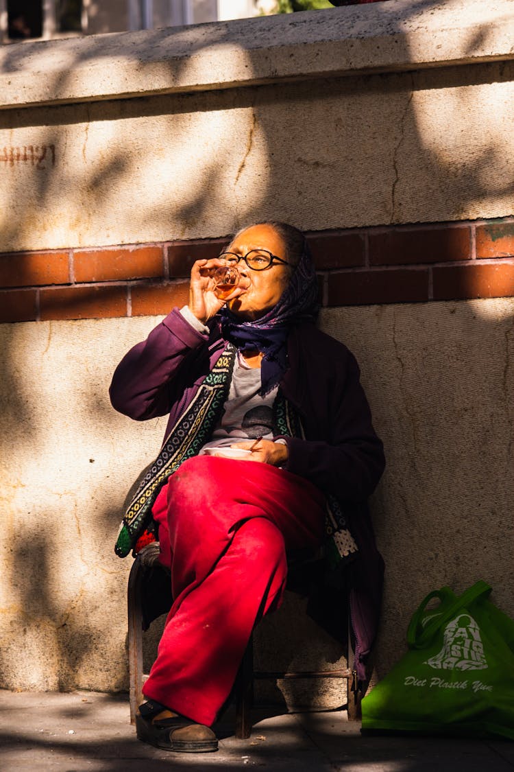 An Elderly Woman Drinking At The Street 