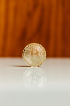 Golden Bitcoin standing upright on a shiny white surface against a wooden background.
