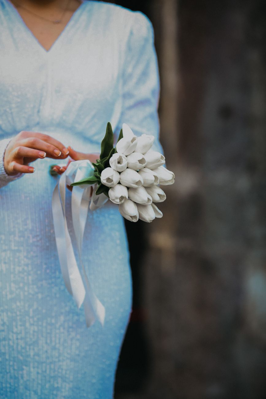 Close-up of a woman in a blue dress holding a bouquet of white tulips, perfect for a wedding theme.