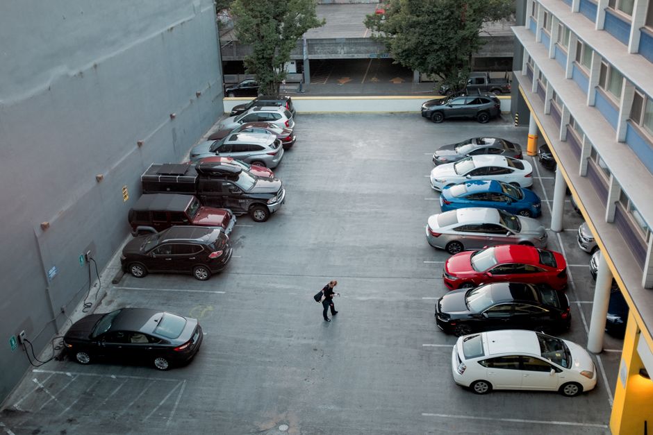 A man walks in a city parking lot filled with various cars, offering a busy urban scene.