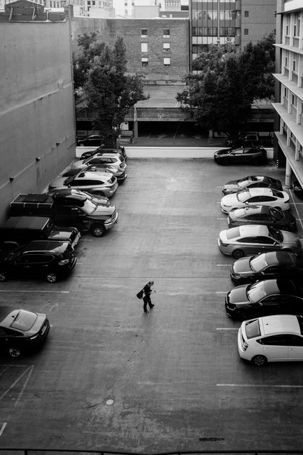 Aerial view of a busy urban parking lot with a lone walker creating a strong contrast.