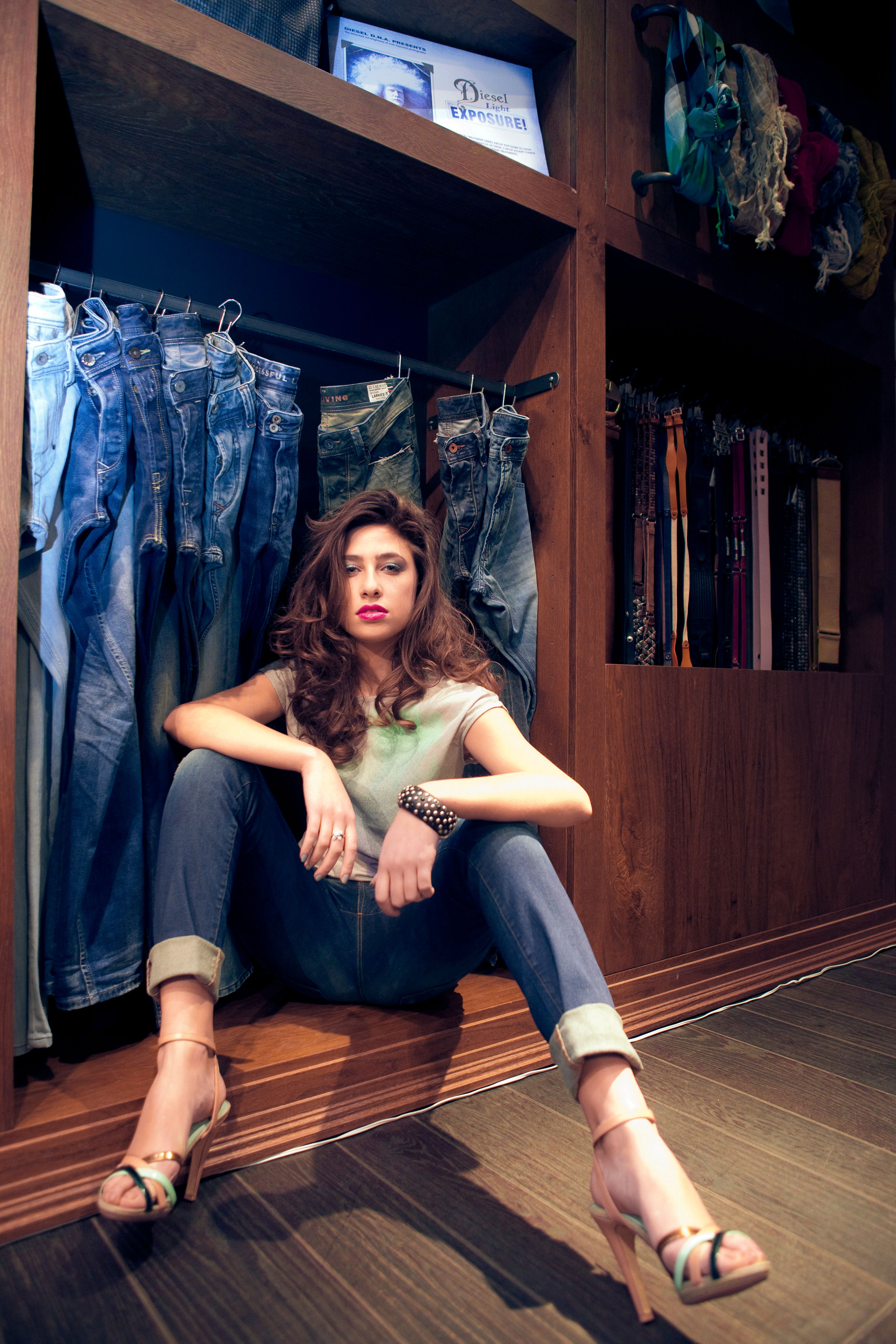 Woman sitting stylishly in a walk-in closet filled with denim jeans and accessories.